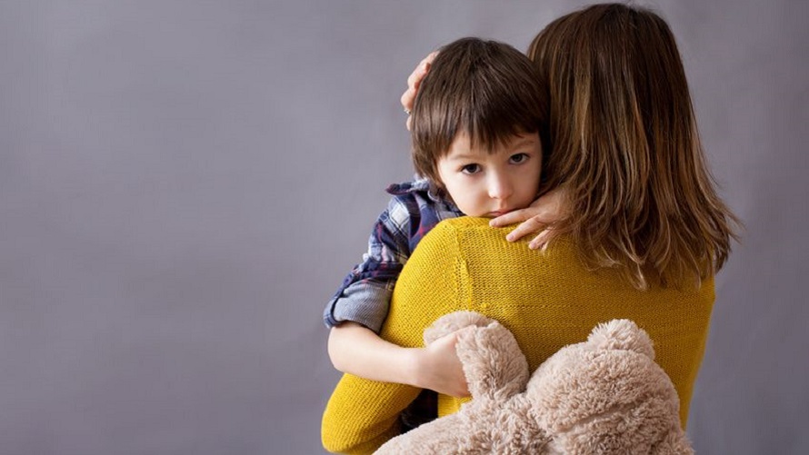 Trauriger Junge Eine Frau hält ihren Jungen über den Schultern, der traurig in die Kamera sieht und seinen Teddy festhält.
